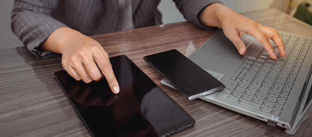 Person using a laptop, tablet, and smartphone while comparing device repair options in Melbourne